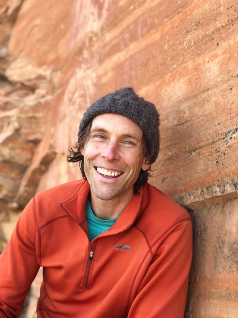 Chris Ingraham in a hat smiling with an outdoor backdrop of red rocks.